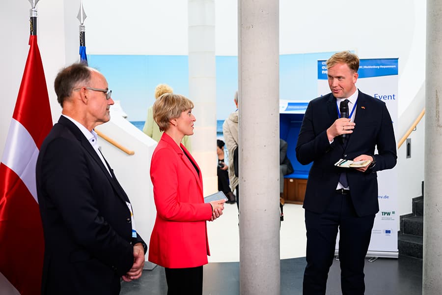 Wirtschaftsminister Viktors Valainis hält ein Mikrophon in der Hand. Zu sehen sind weiter Moderatorin Marianna Evenstein und Wirtschaftsminister Dr. Wolfgang Blank. Wirtschaftsminister Viktors Valainis hält ein Mikrophon in der Hand. Zu sehen sind weiter Moderatorin Marianna Evenstein und Wirtschaftsminister Dr. Wolfgang Blank.
